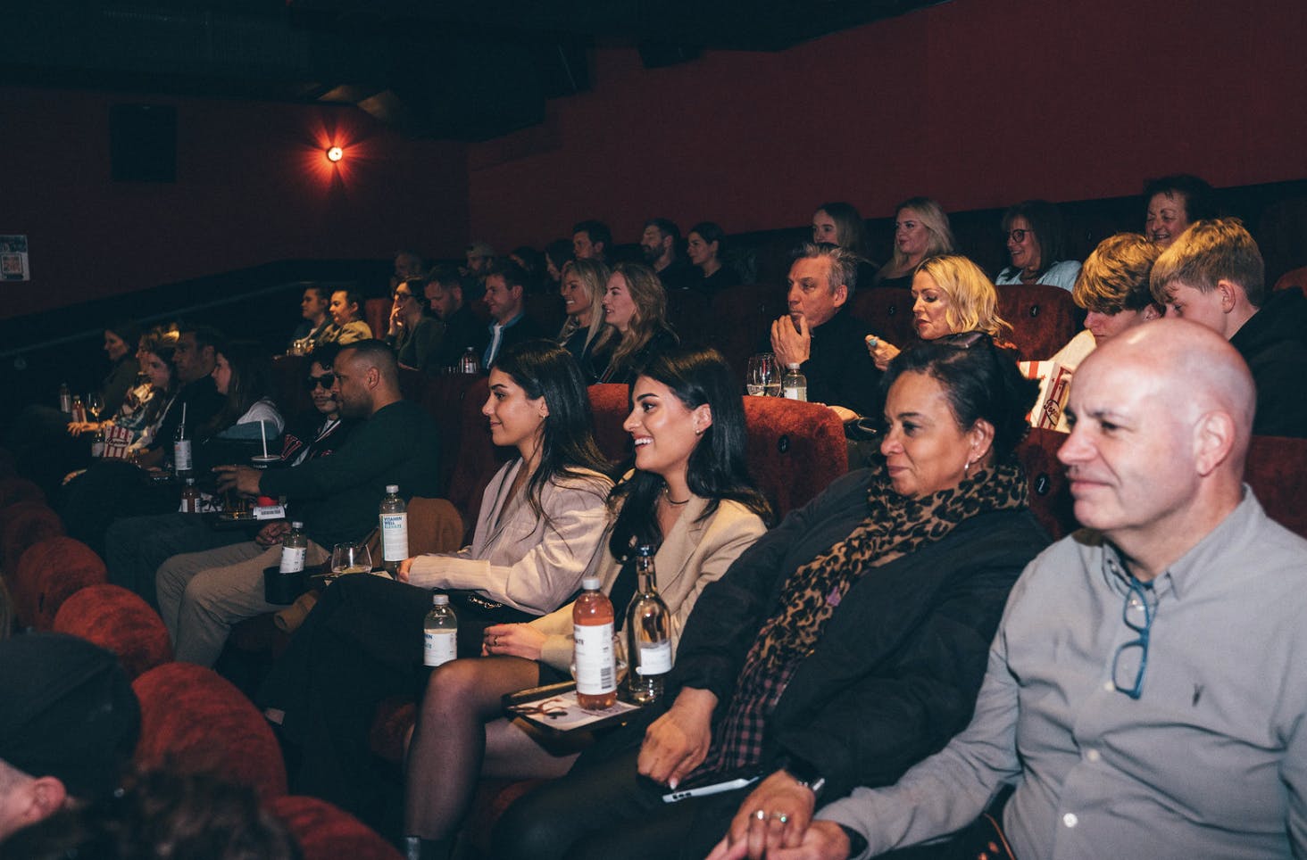 Guests enjoy drinks while smiling in a cinema screen.