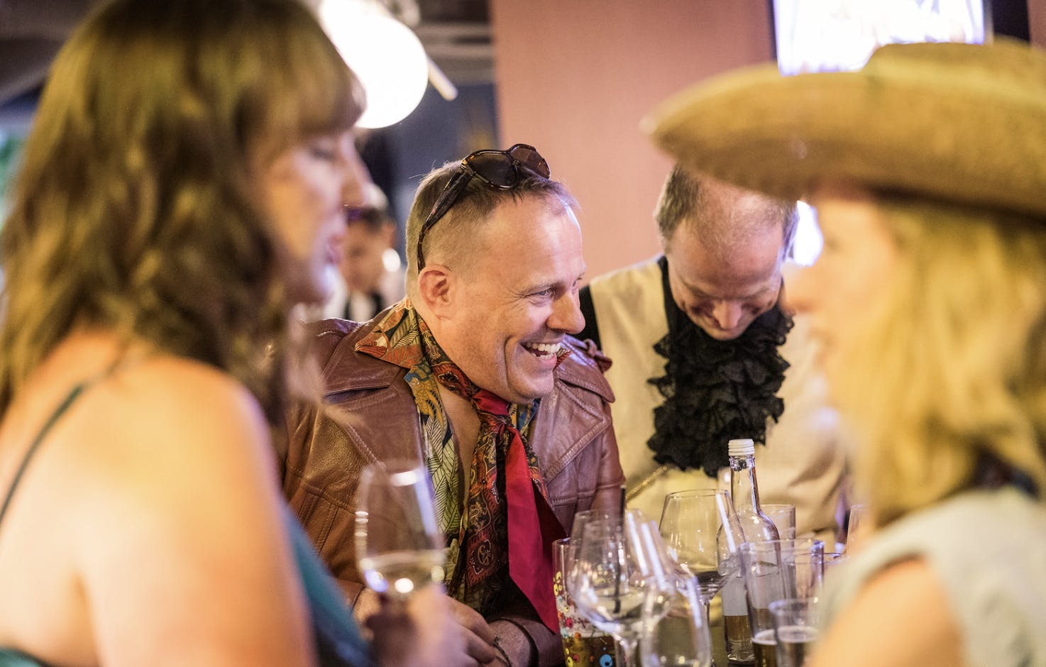 Smiling guests in 80s fancy dress laugh over drinks.