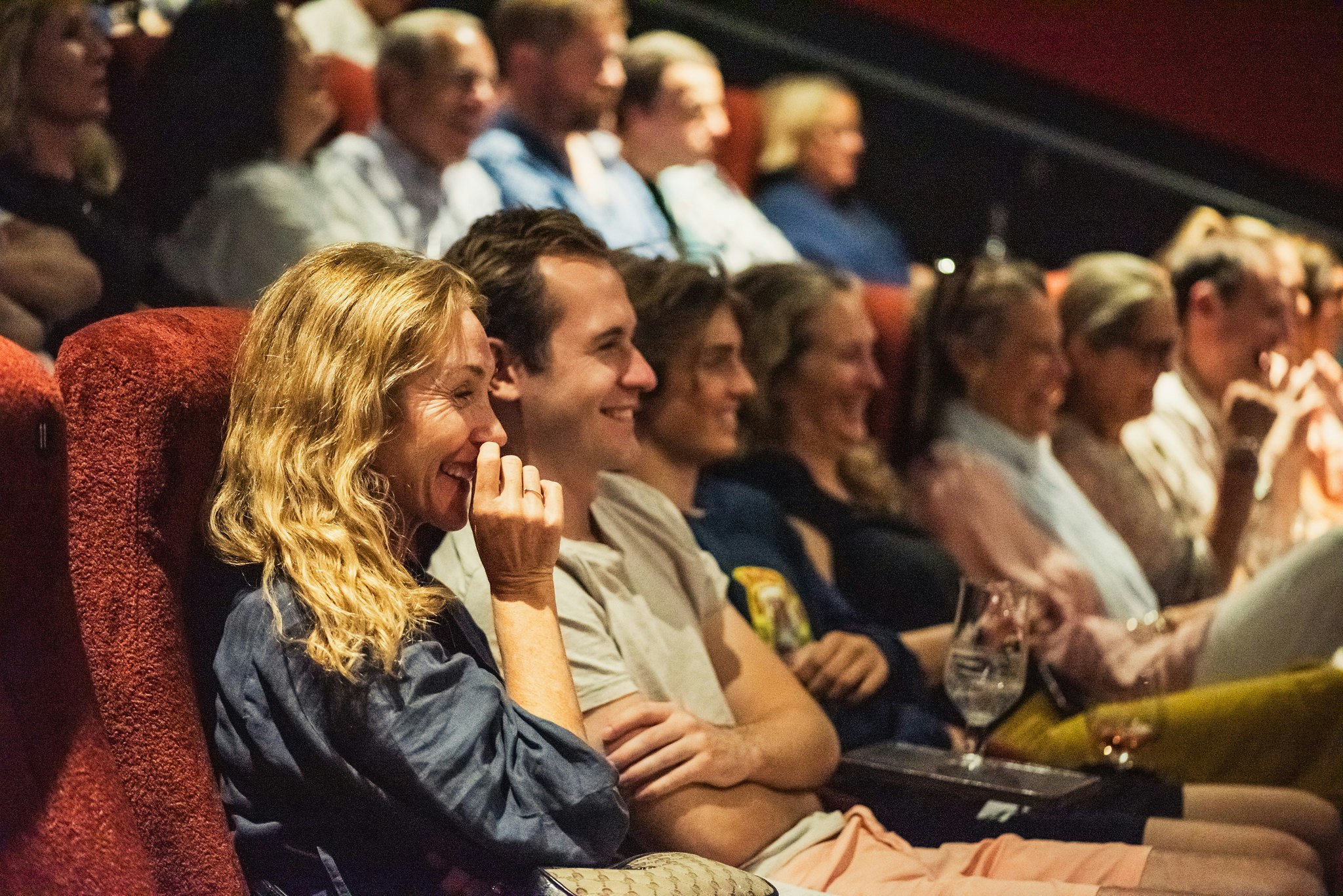 An audience laughs, with a woman visibly moved as they watch guests on stage.