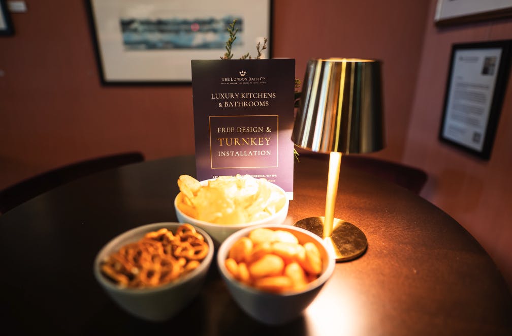 A selection of complimentary snacks on a wood table, with a London Bath Co advert nearby.