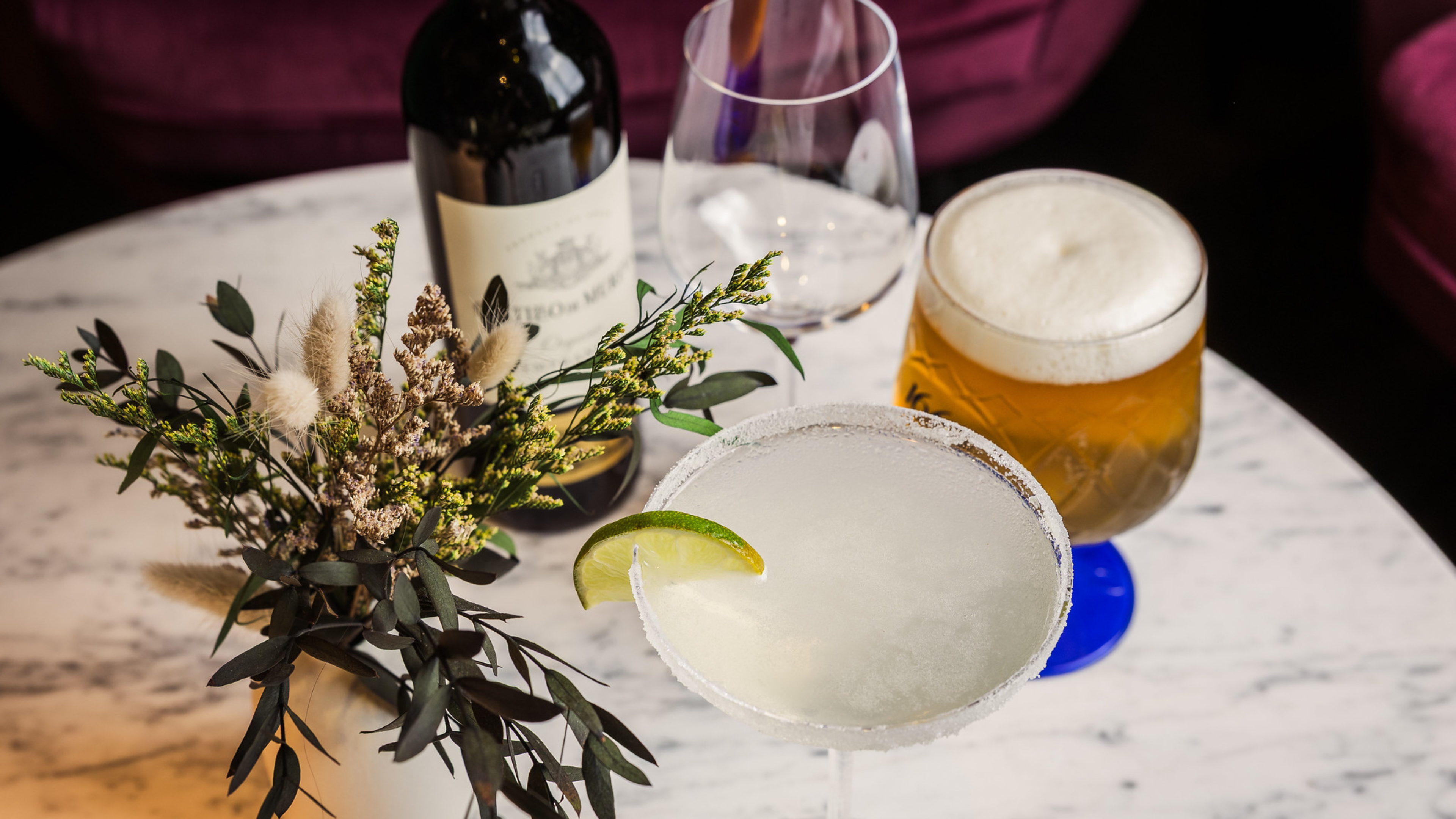 A marble table of drinks is laid out for guests with a vibrant floral centrepiece. 