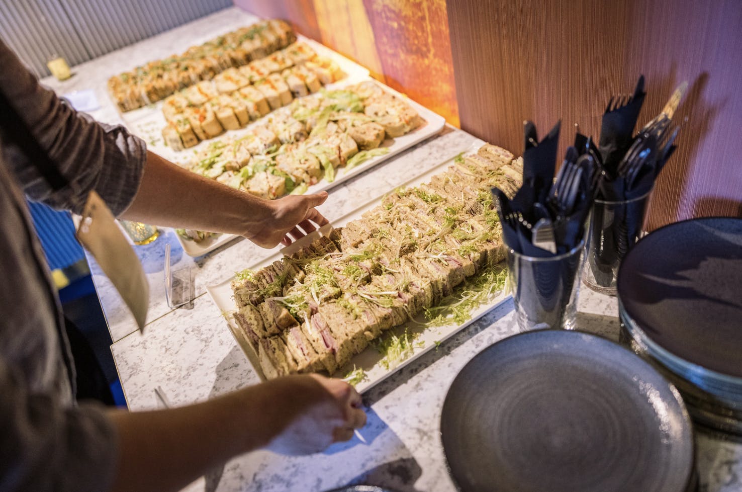 A staff member adds more trays of sandwiches to a large buffet.