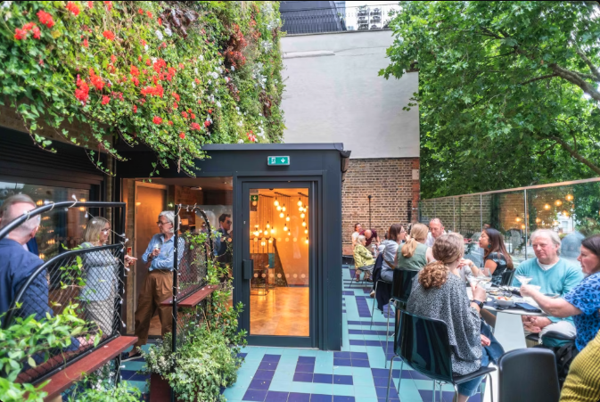 The cinema's green and floral sun terrace filled with patrons enjoy a drink on a Summer's day.