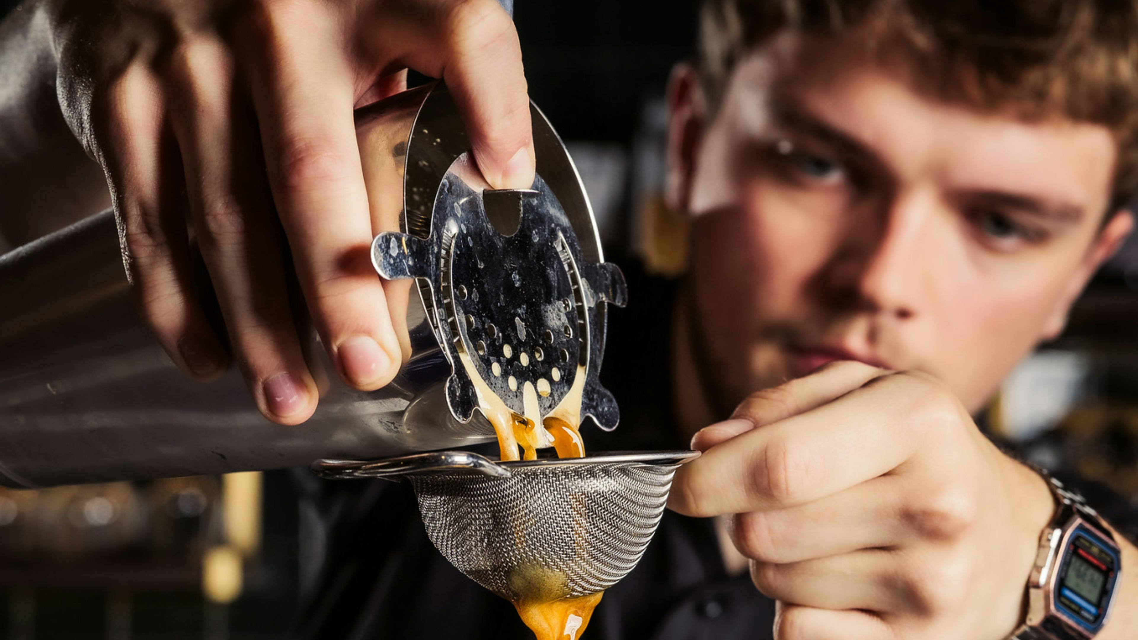 A member of staff pours and espresso martini carefully through a strainer into a glass.