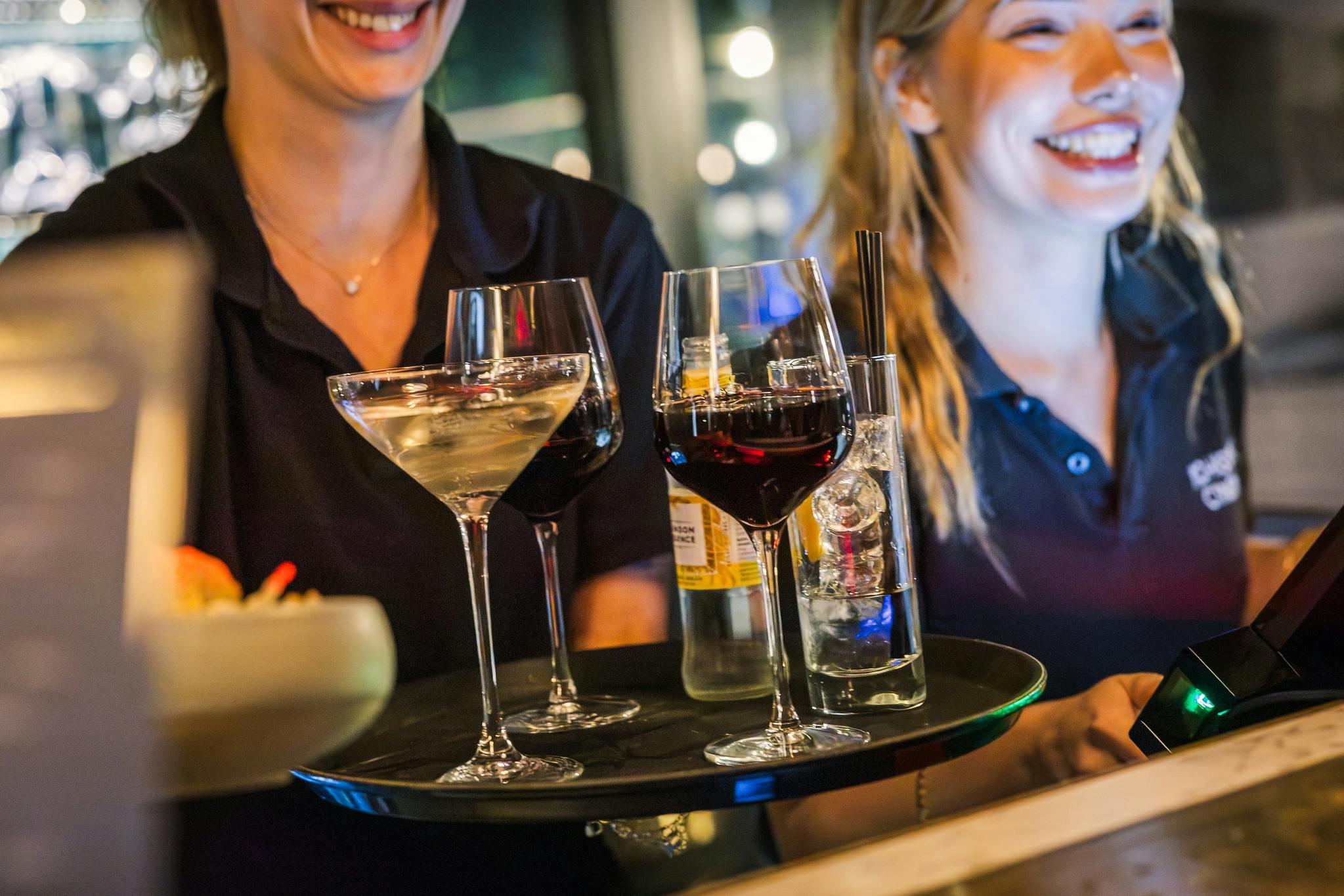 Smiling staff handing over a tray of drinks including wine.