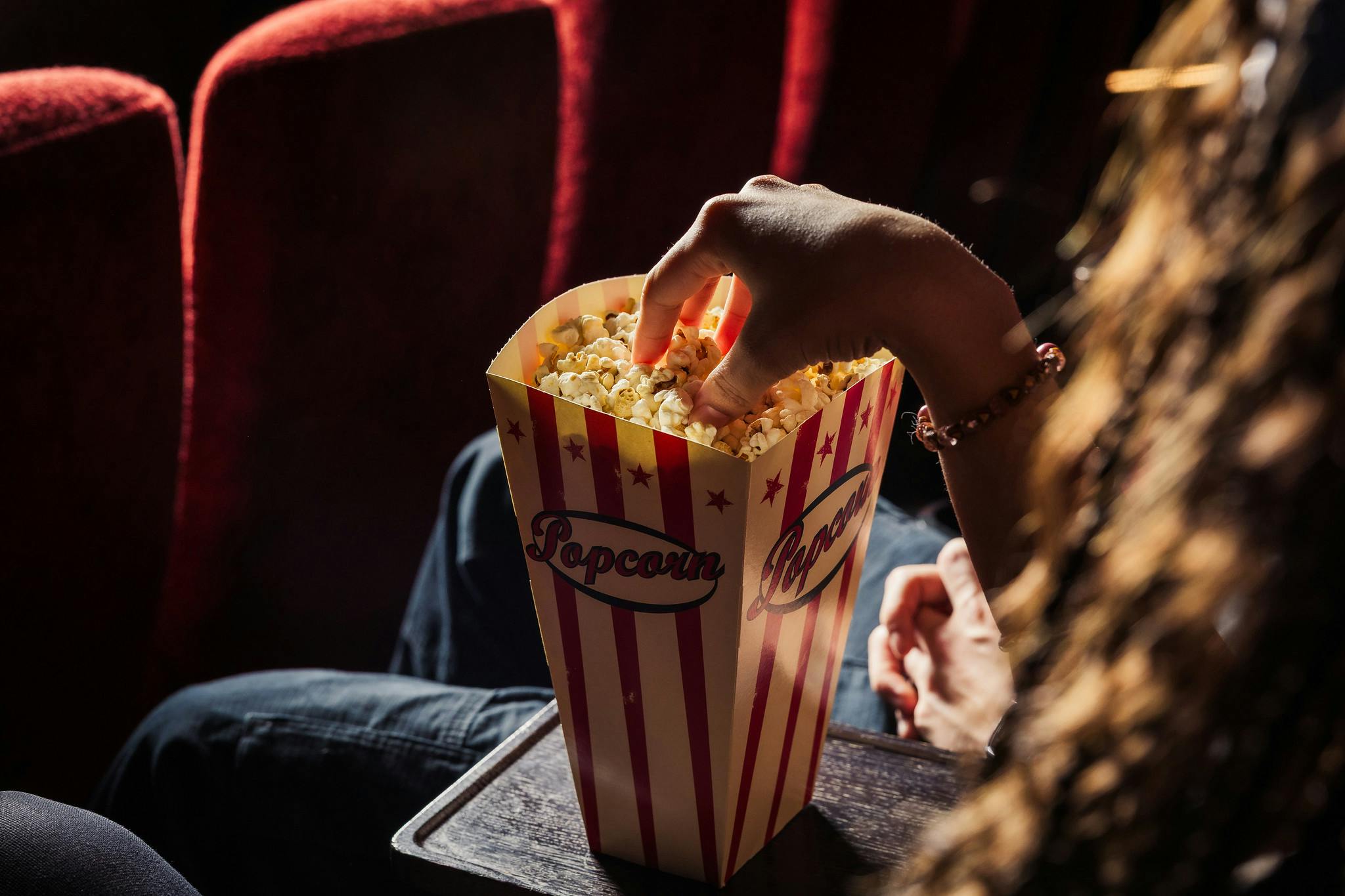 A hand dips into a large bucket of popcorn in a cinema screen.