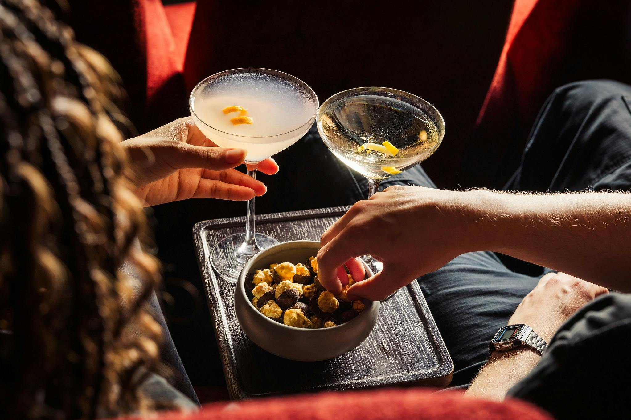 Two customers enjoy cocktails and gourmet popcorn in a cinema screen.