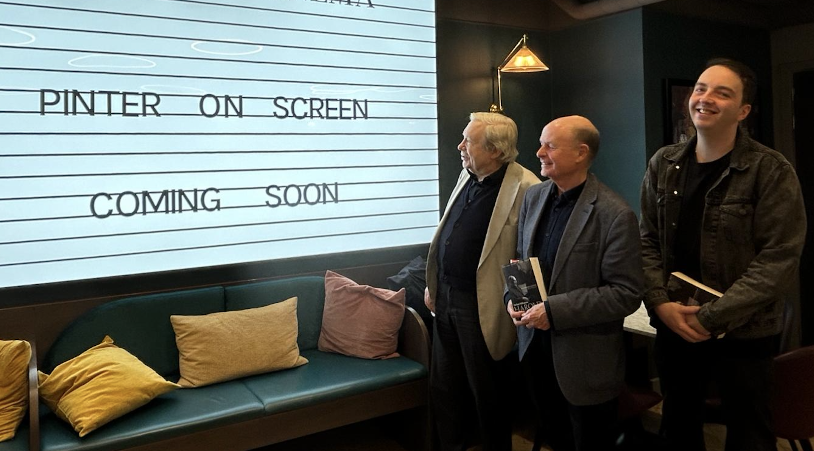 Three men smile next to the cinema readograph, announcing a new film season.