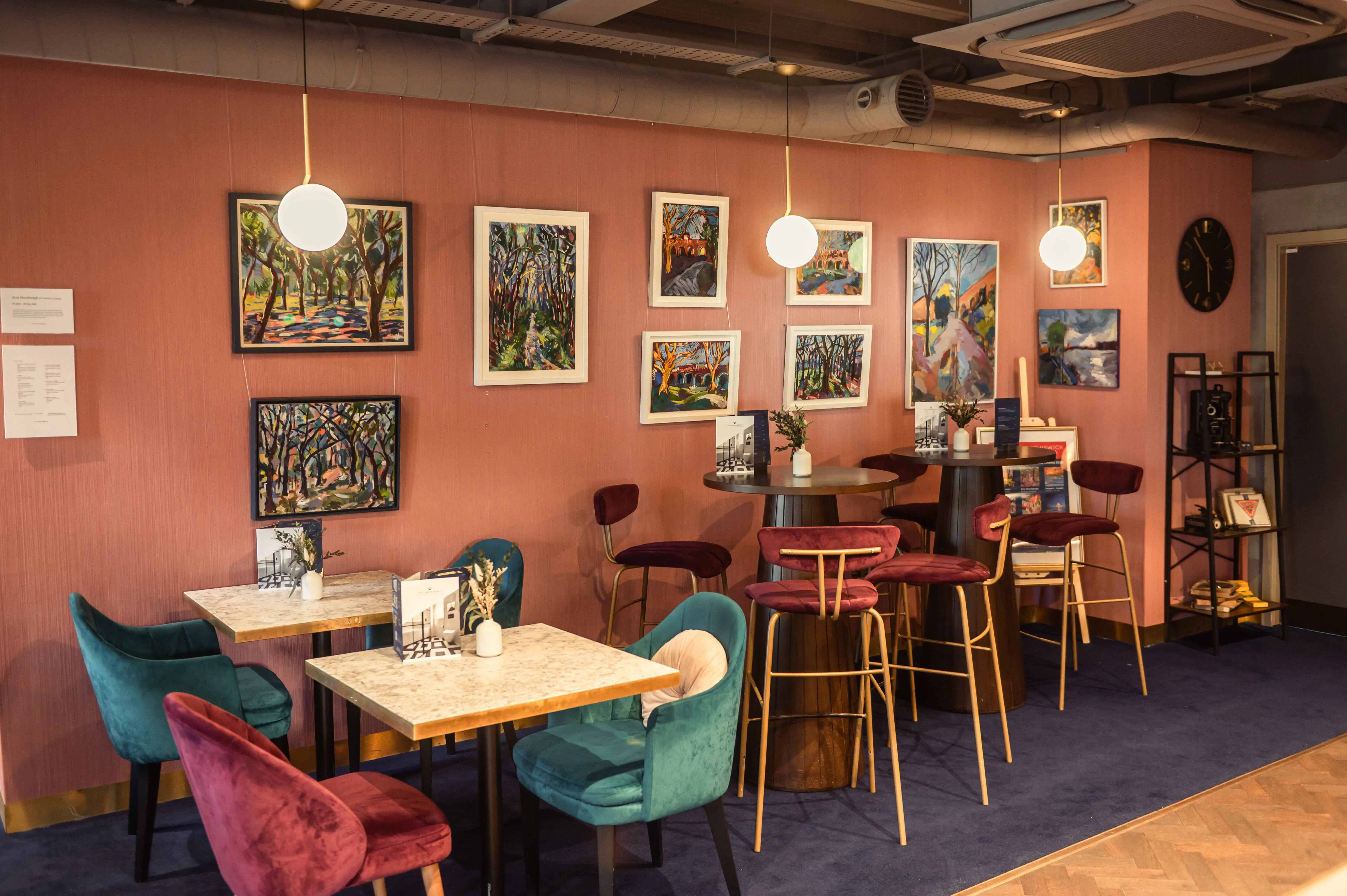 Two people enjoy a drink in the Lounge bar with some floral artworks displayed in a gallery behind them.