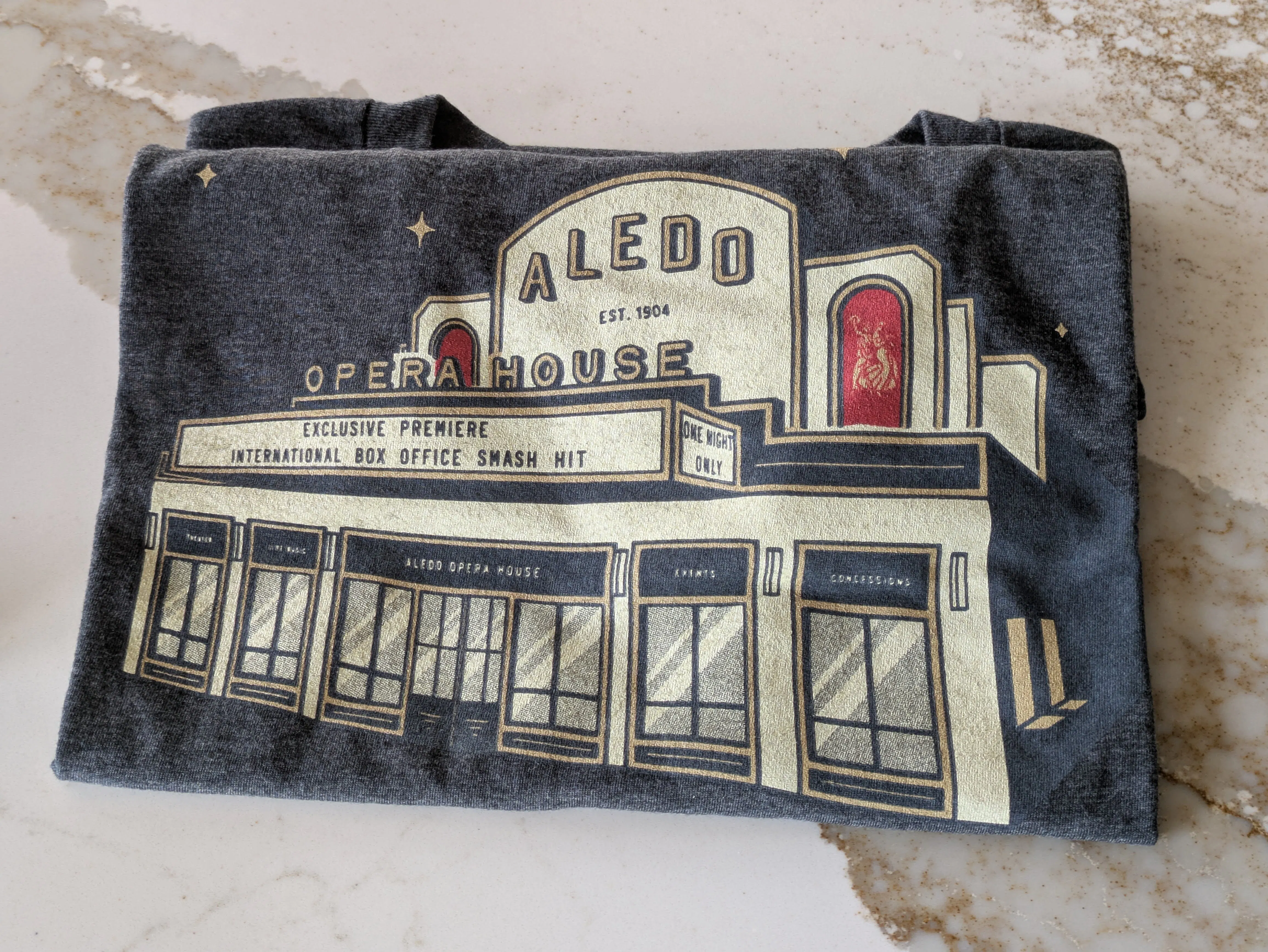 a charcoal black t-shirt with the Aledo Opera House building design printed on the front